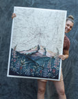 Katie Jeanne Reim of Final Switchback holding one of her large Giclee prints against a blue backdrop