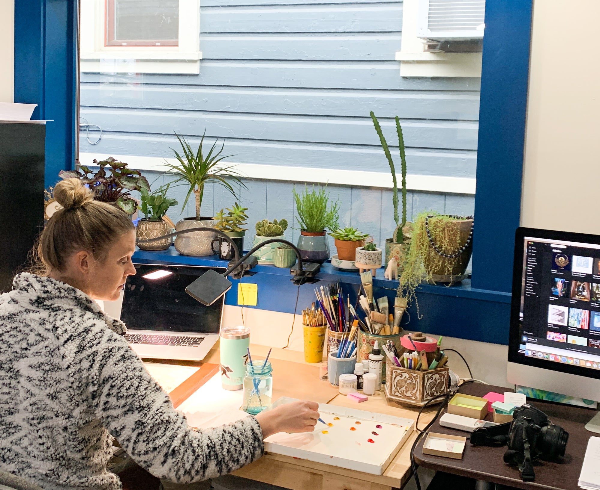 Artist Katie Jeanne Reim, outdoor and nature-inspired artist from Final Switchback painting nature scenes at her desk.