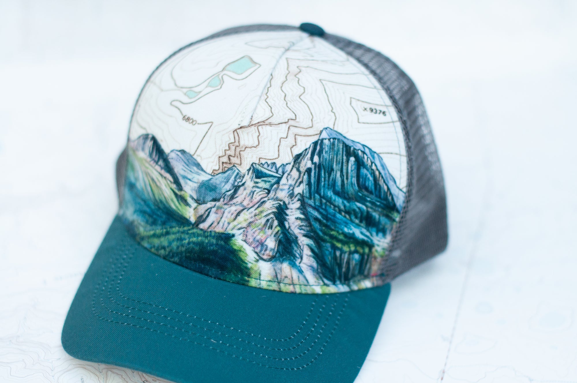 front angle view of the final switchback trucker hat featuring artist Katie Jeanne Reim&#39;s Glacier Grinnell print