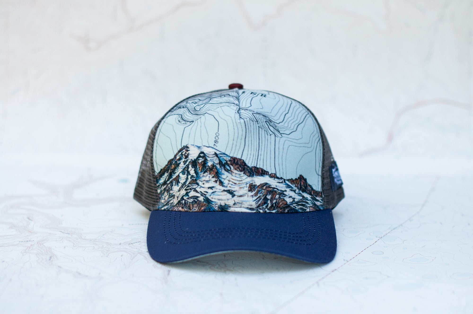 front view of the final switchback trucker hat featuring artist Katie Jeanne Reim&#39;s Mount Rainier Summit print