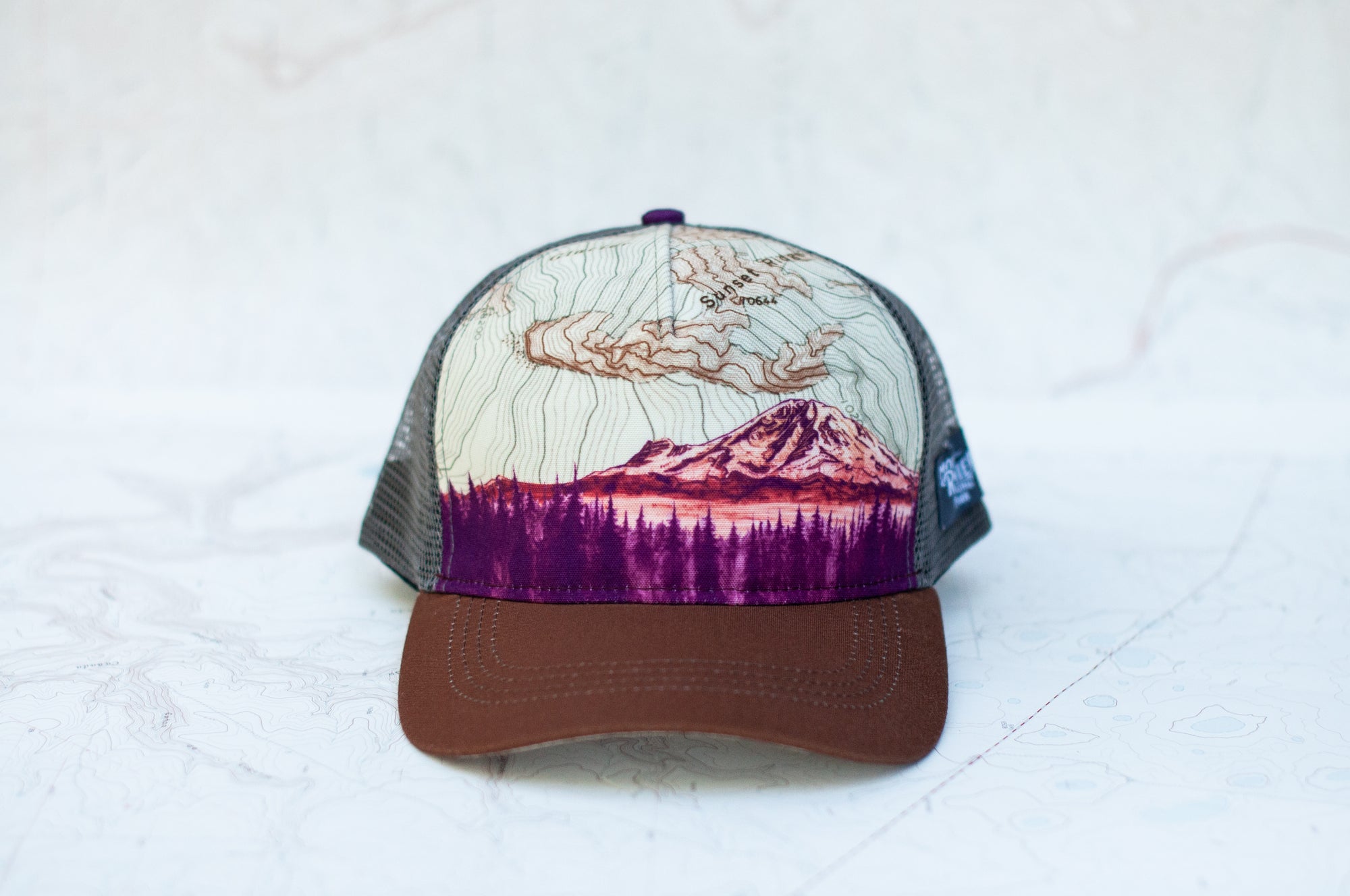front view of the final switchback trucker hat featuring artist Katie Jeanne Reim&#39;s Mount Rainier Sunset print