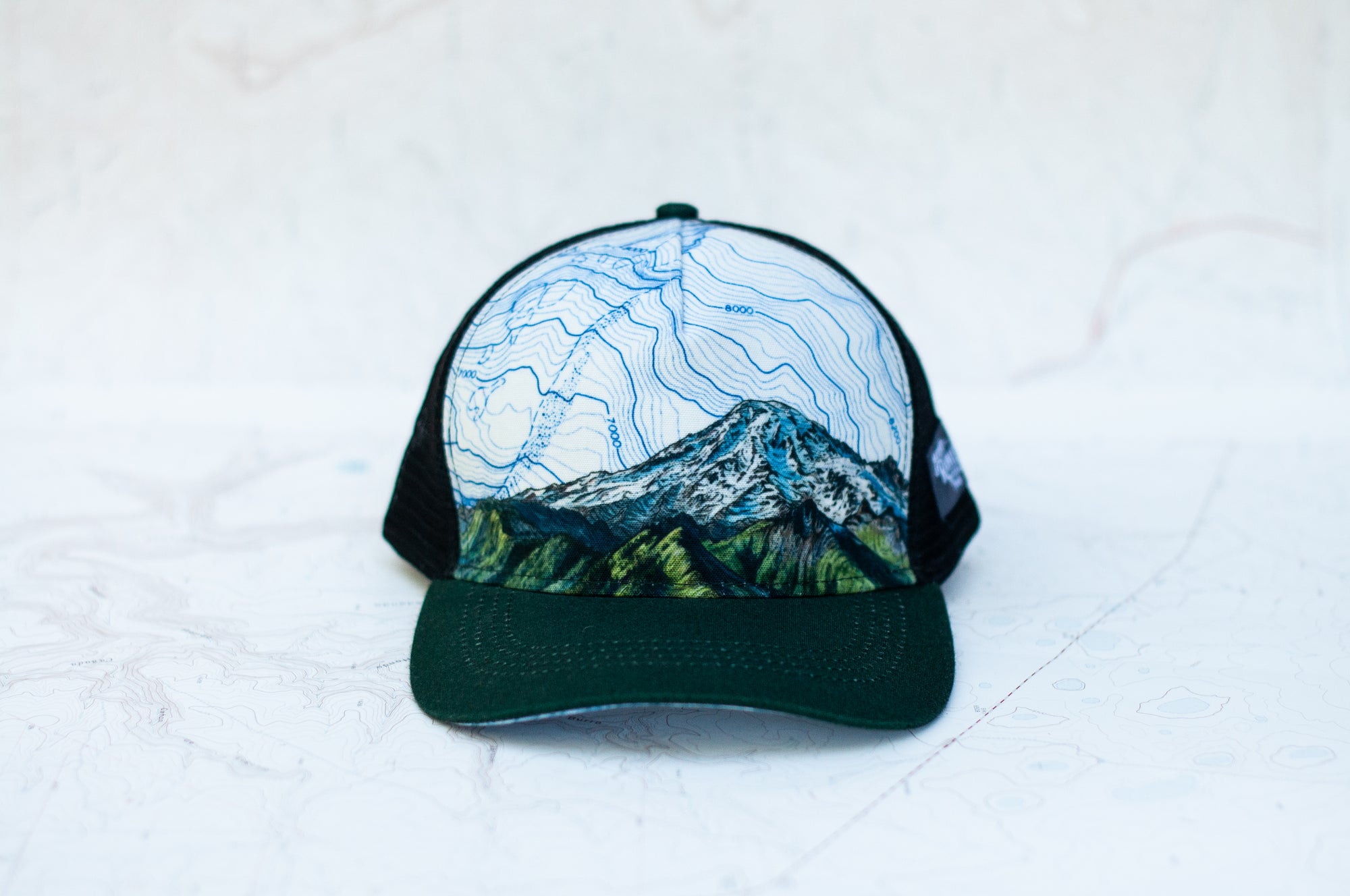 front view of the final switchback trucker hat featuring artist Katie Jeanne Reim&#39;s Mount Rainier Tatoosh print