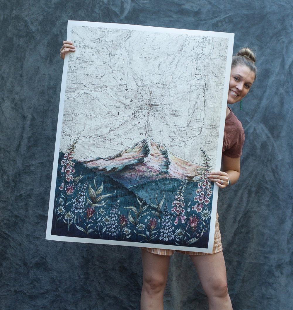 Katie Jeanne Reim of Final Switchback holding one of her large Giclee prints against a blue backdrop