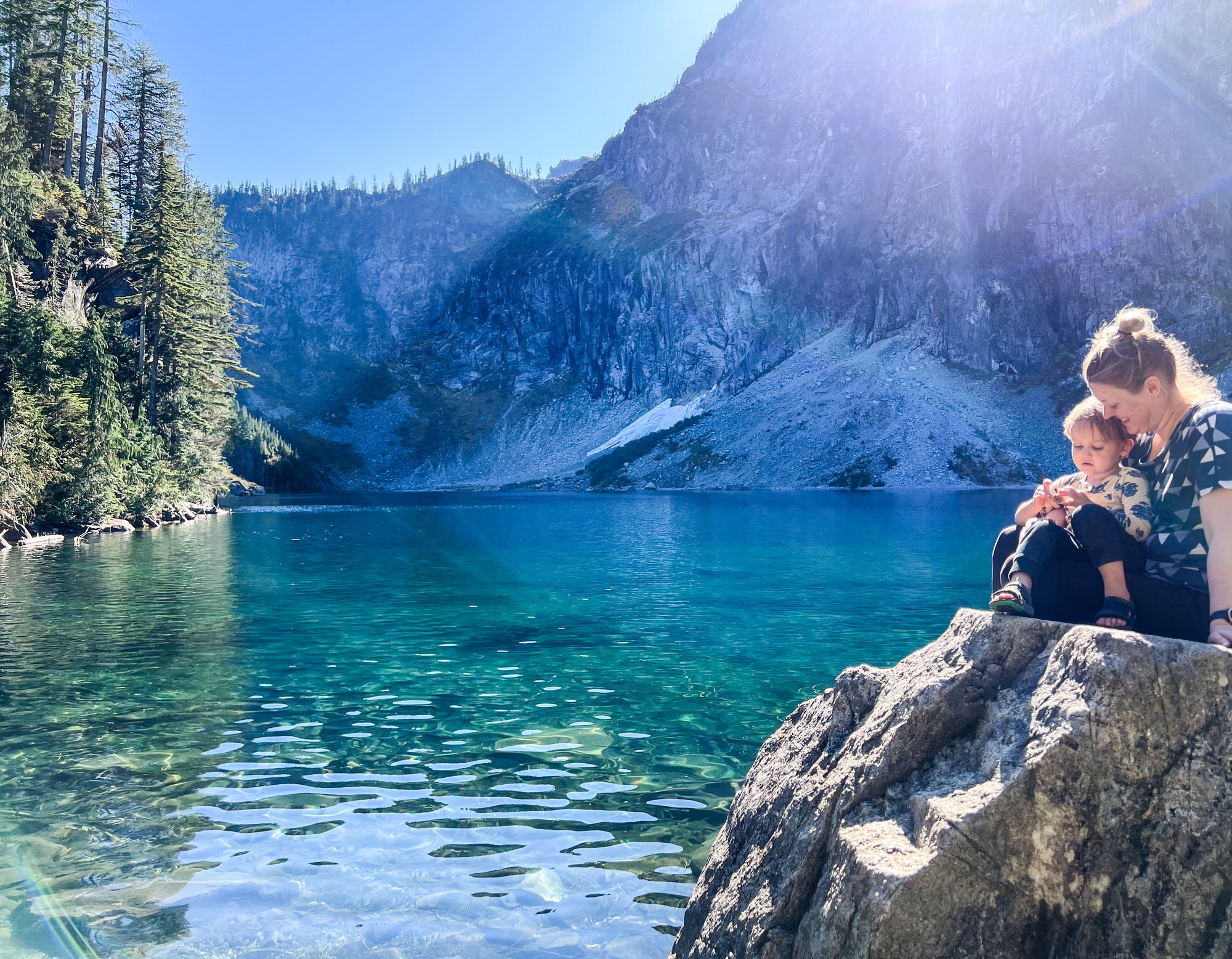 Katie Reim, outdoor and nature-inspired artist from Final Switchback and her son sitting on a rock on a crystal turquoise lake and mountain setting